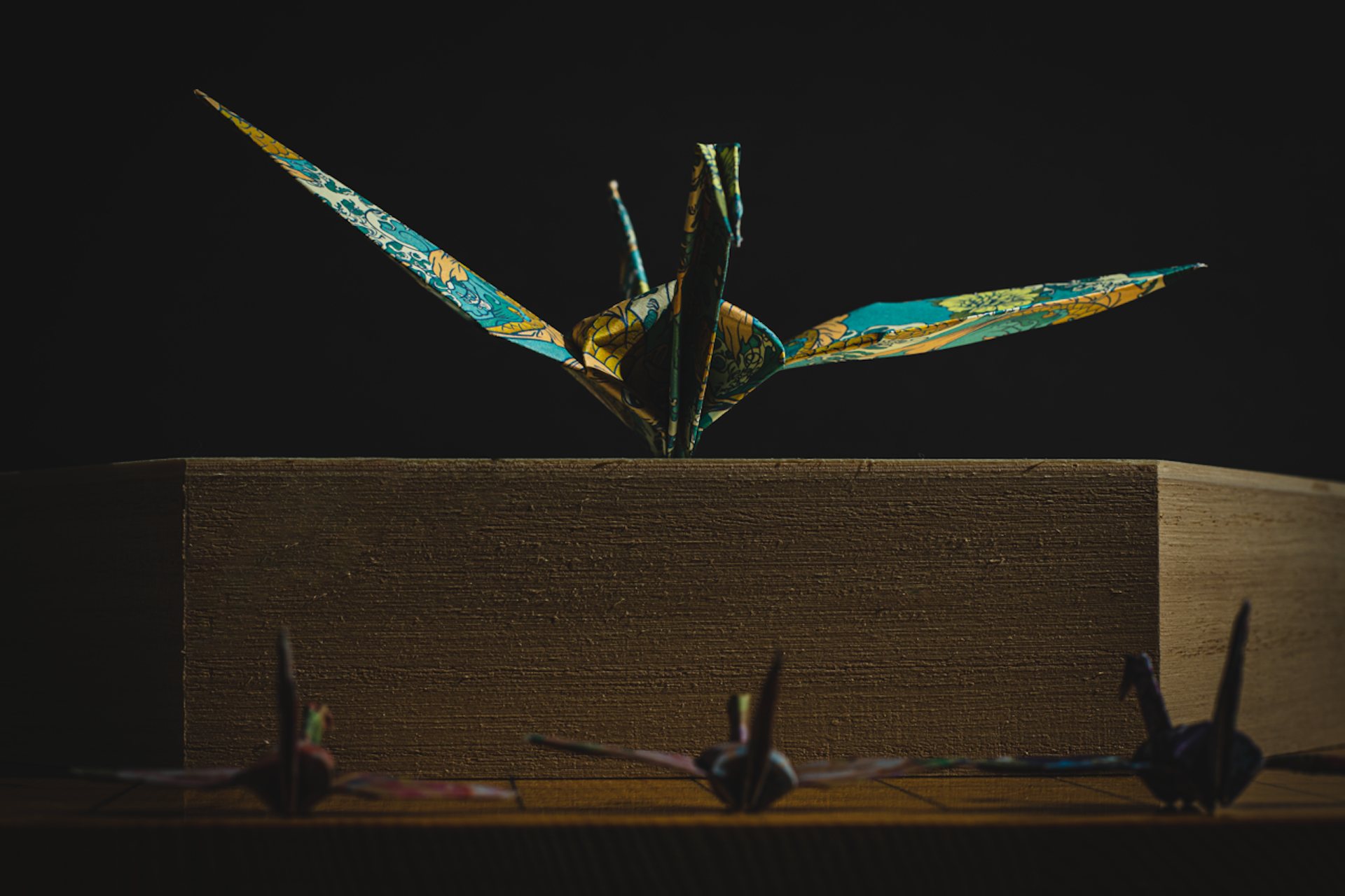 Origami cranes on wooden box, dark dramatic