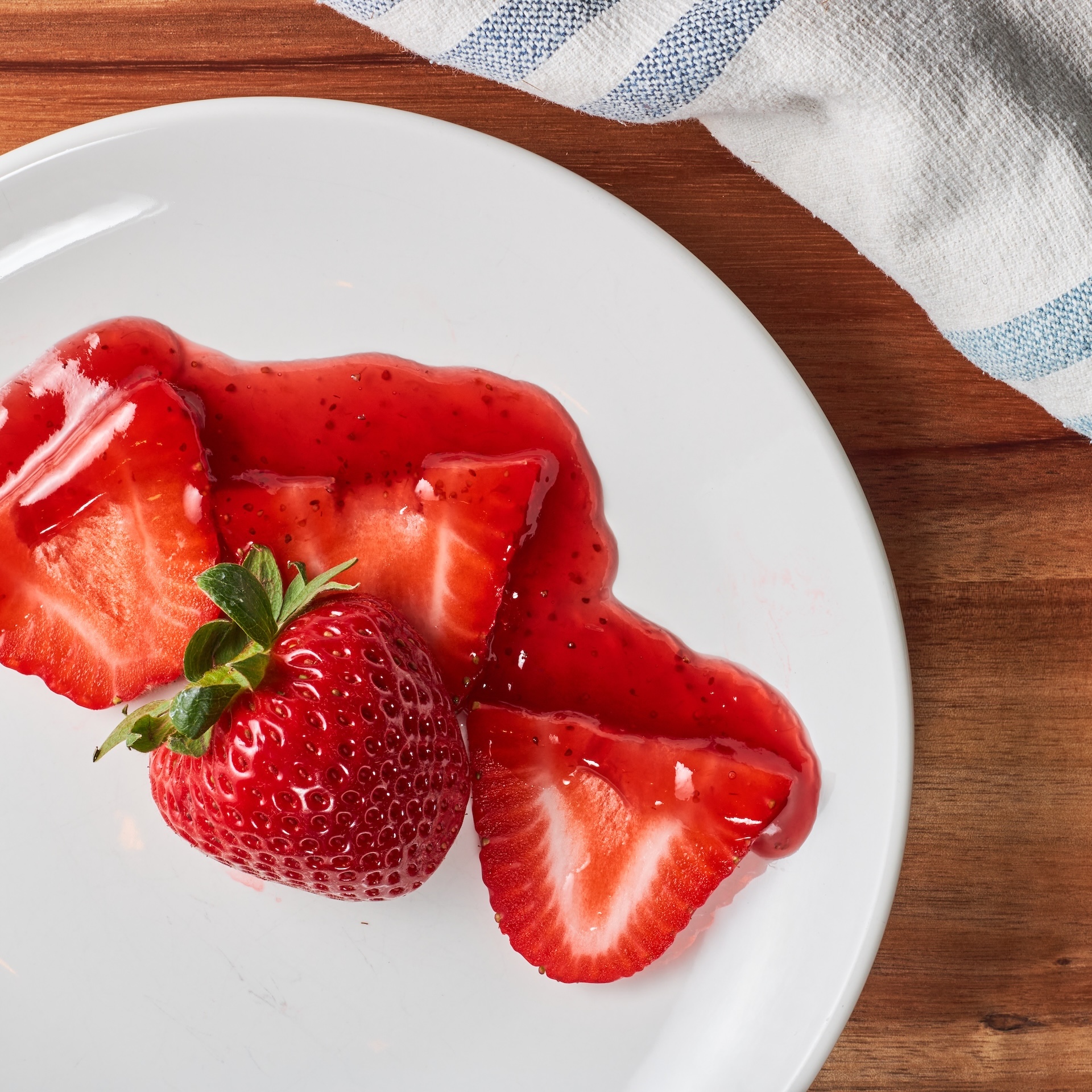 Fresh strawberries on white plate, wooden surface